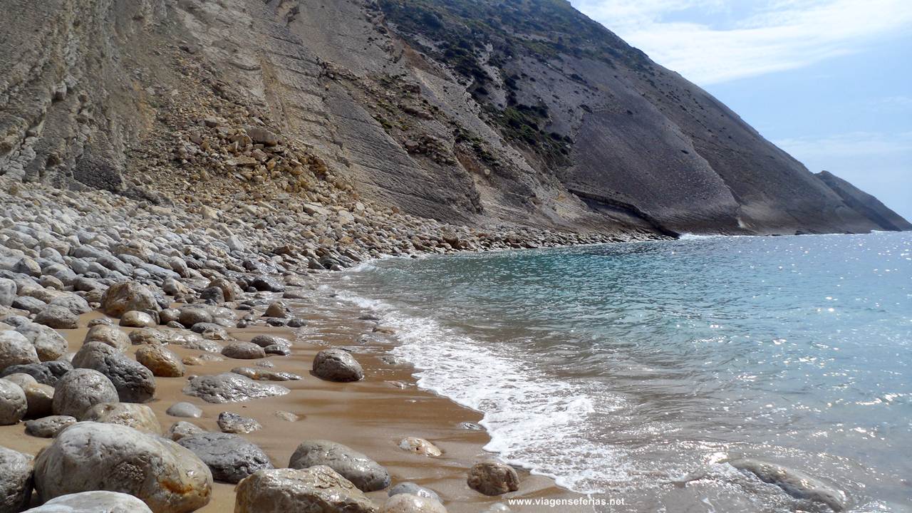 Junto à água na praia dos Lagosteiros com a Pedra da Mua (escarpa sul)